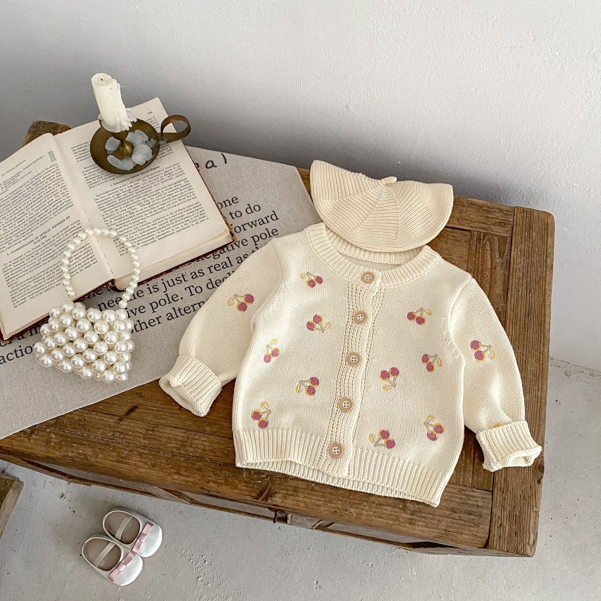 Baby sweater with cherry pattern on a wooden surface with books and shoes.