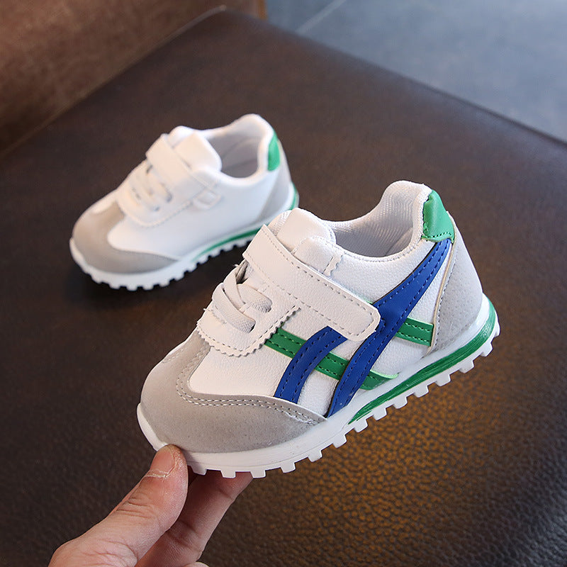 White children's sneakers with blue and green accents on a dark surface