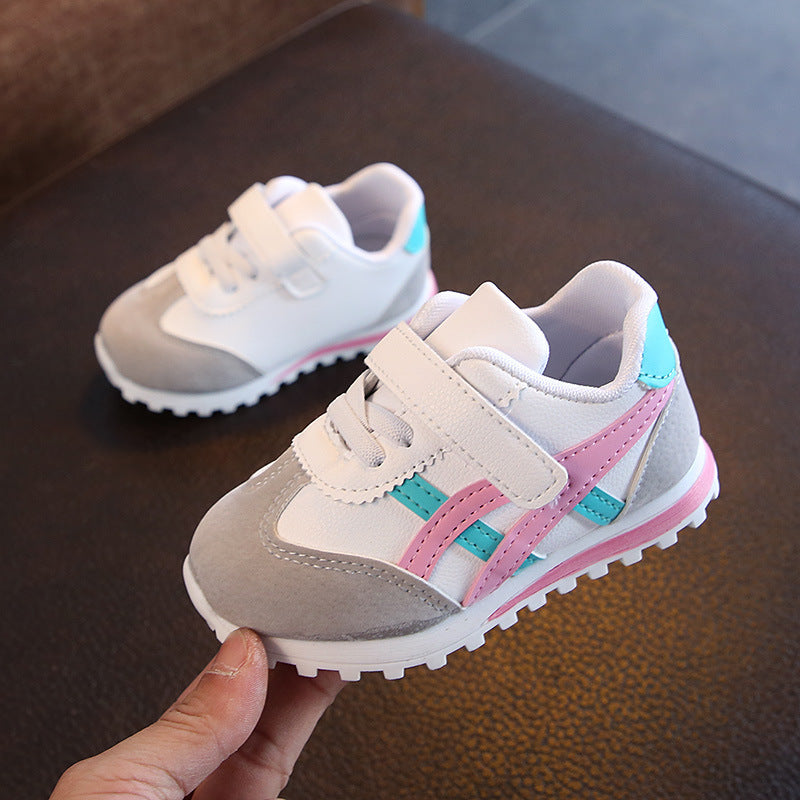 Children's sneakers with gray, pink, and blue design held by a hand on a dark surface.