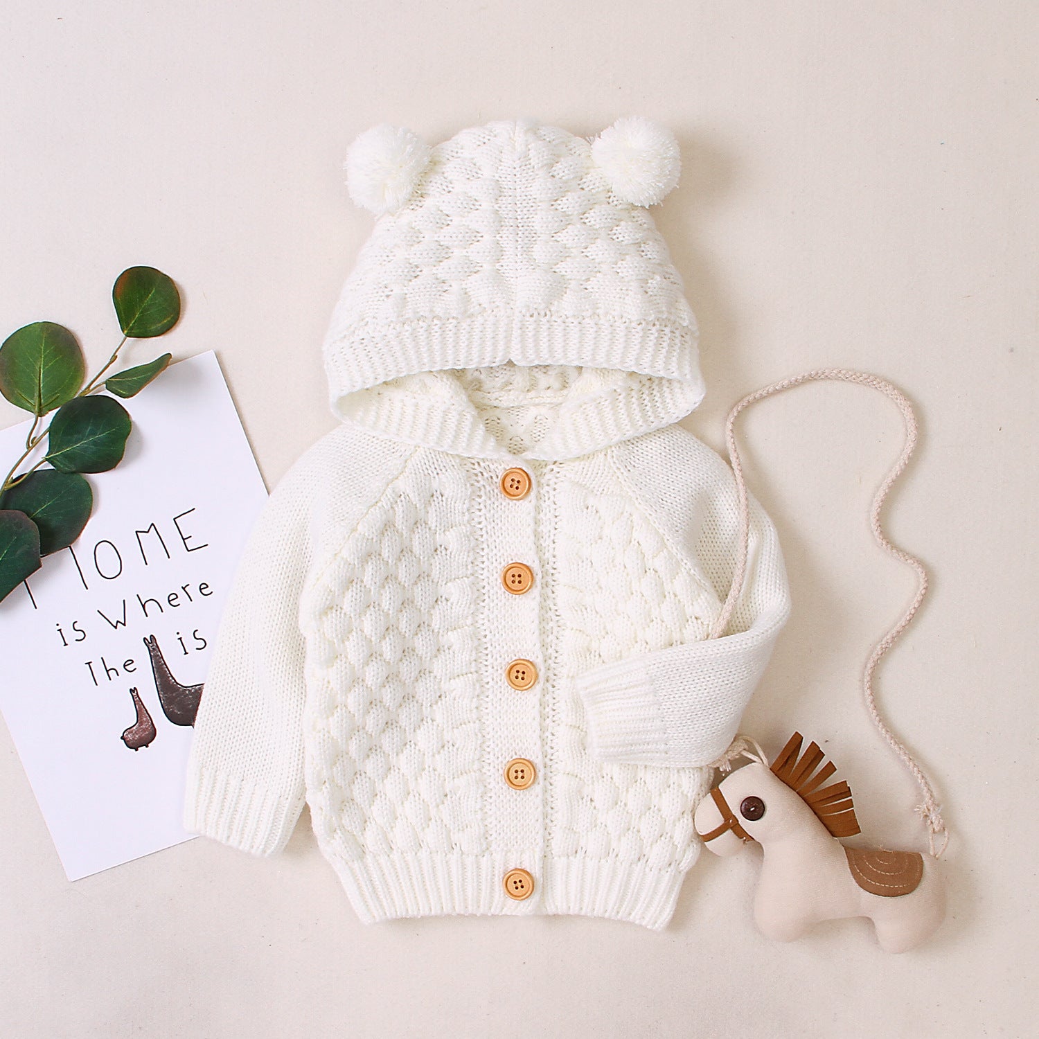 White knitted baby outfit with a hat and cardigan on a light background