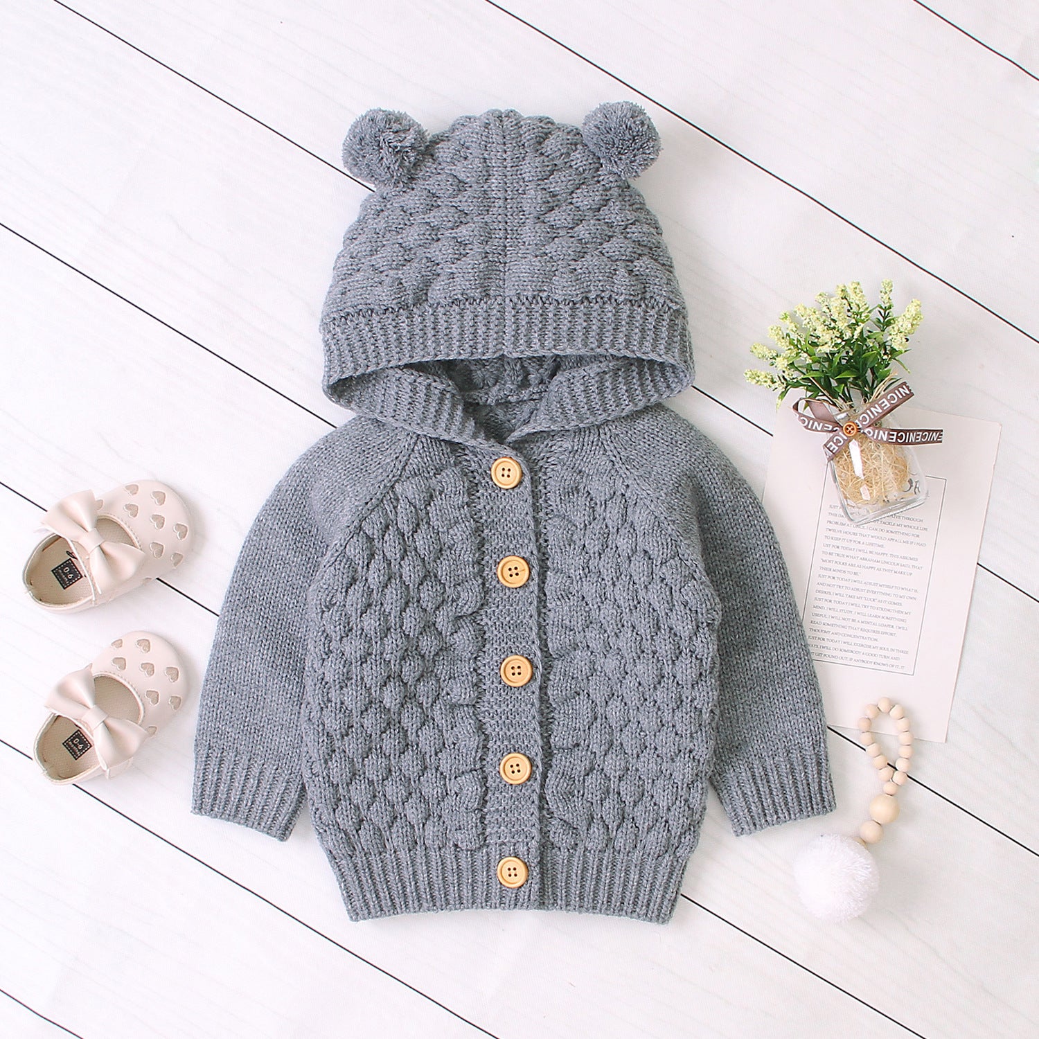 Gray knitted baby cardigan with bear ears on a white wooden floor.