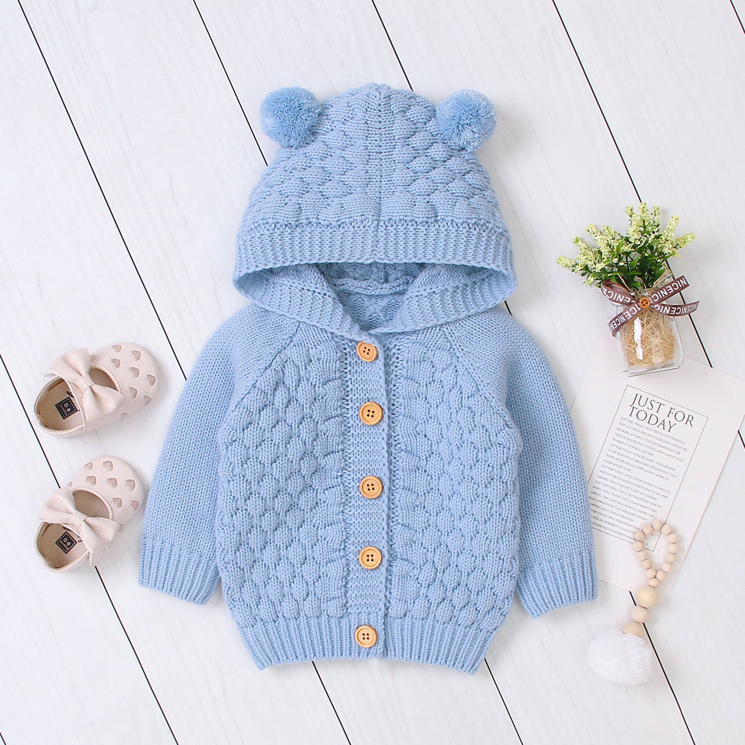 Blue knitted baby cardigan with hood on a white wooden floor.