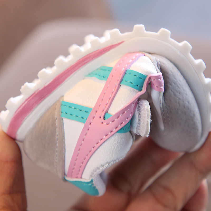 Close-up of a baby shoe with pink and blue accents held in a hand.