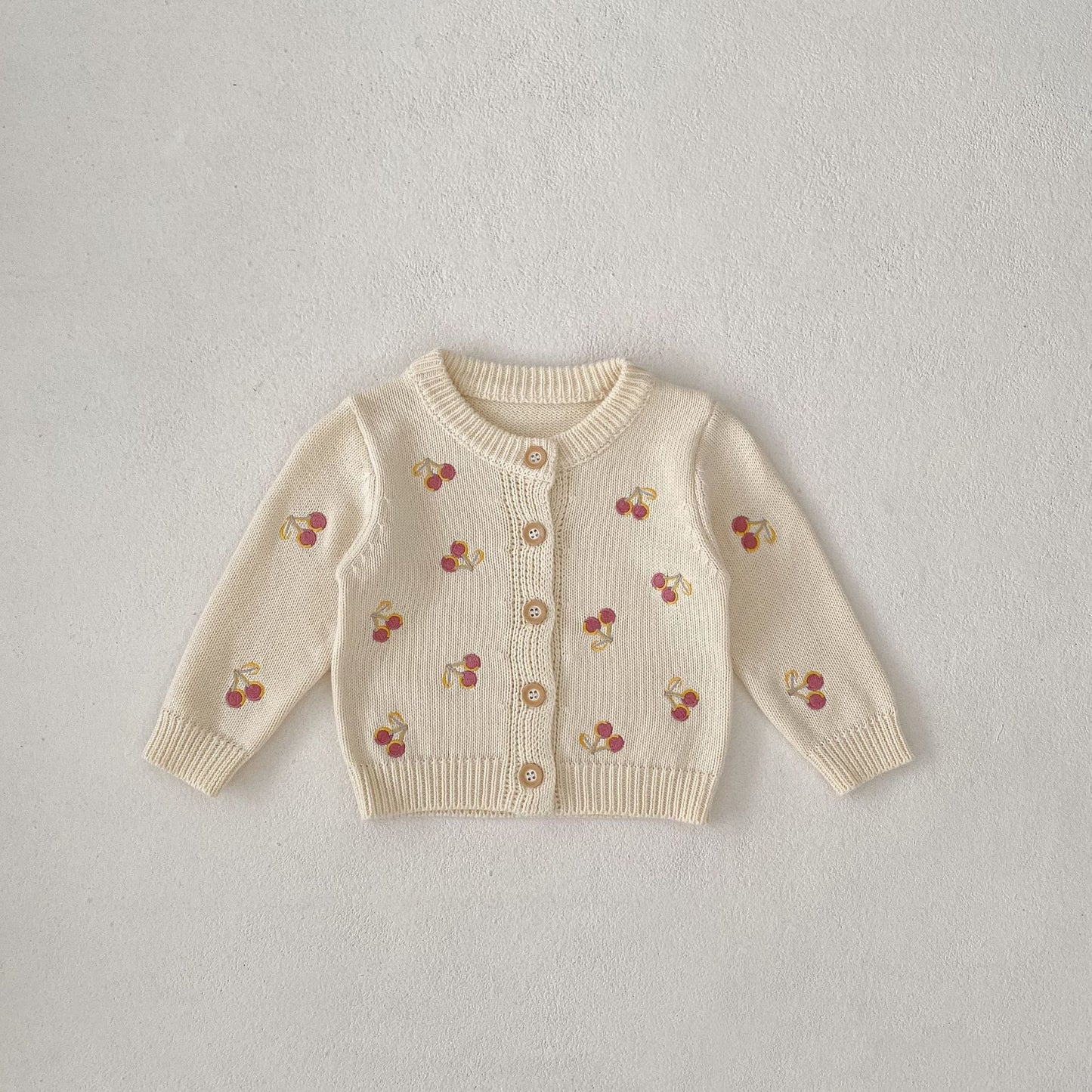 Beige cardigan with cherry patterns on a light gray background