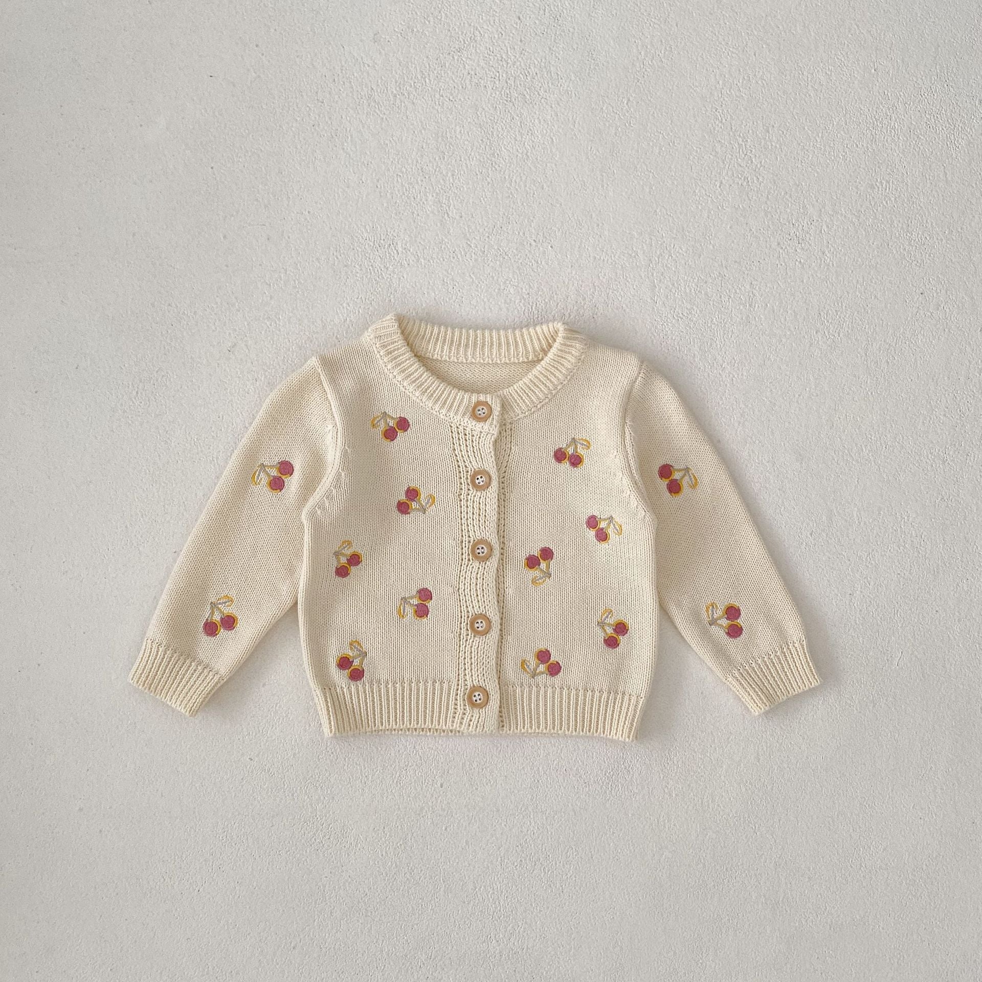 Beige cardigan with cherry patterns on a light gray background