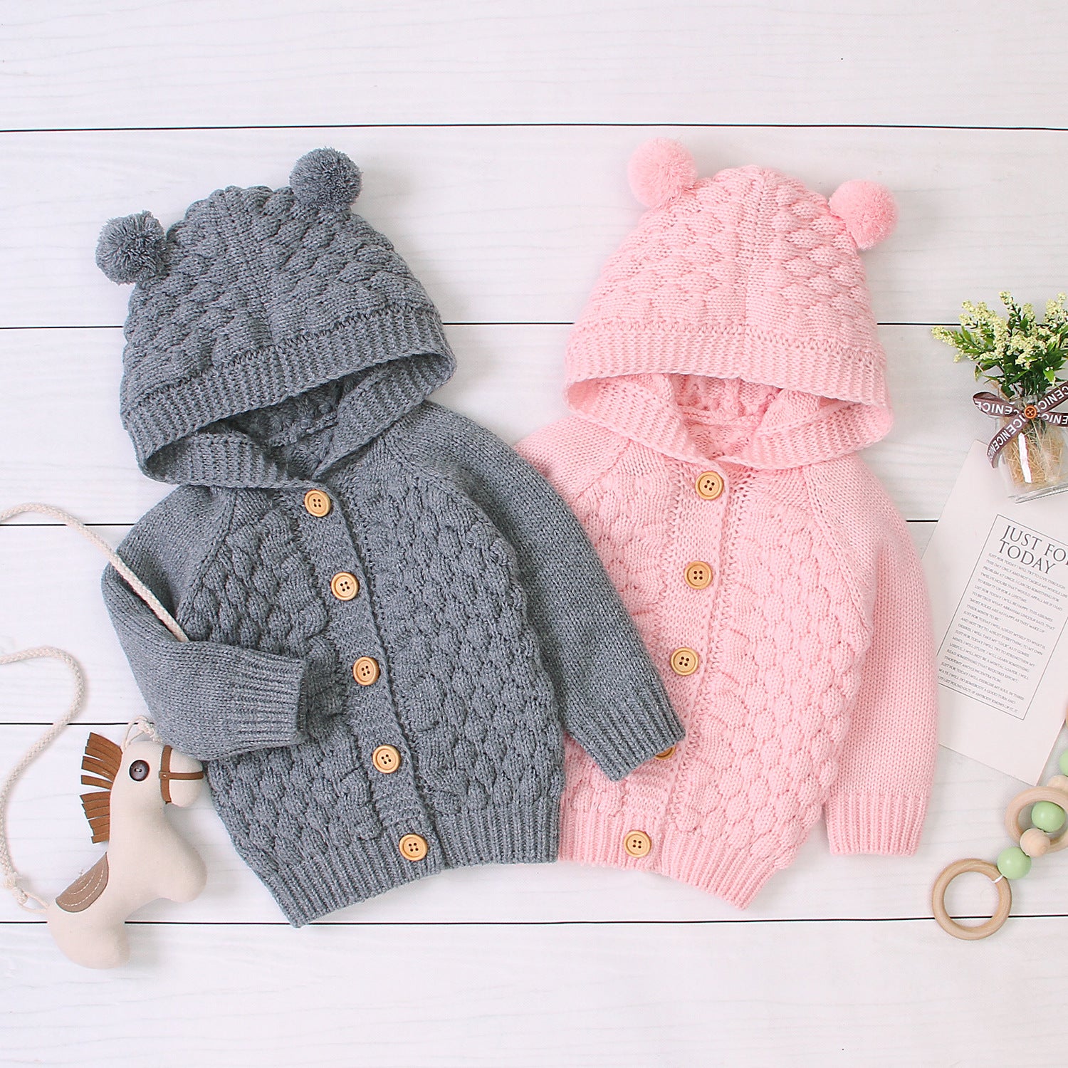 Gray and pink knitted baby cardigans with hoodies on a light wooden surface.