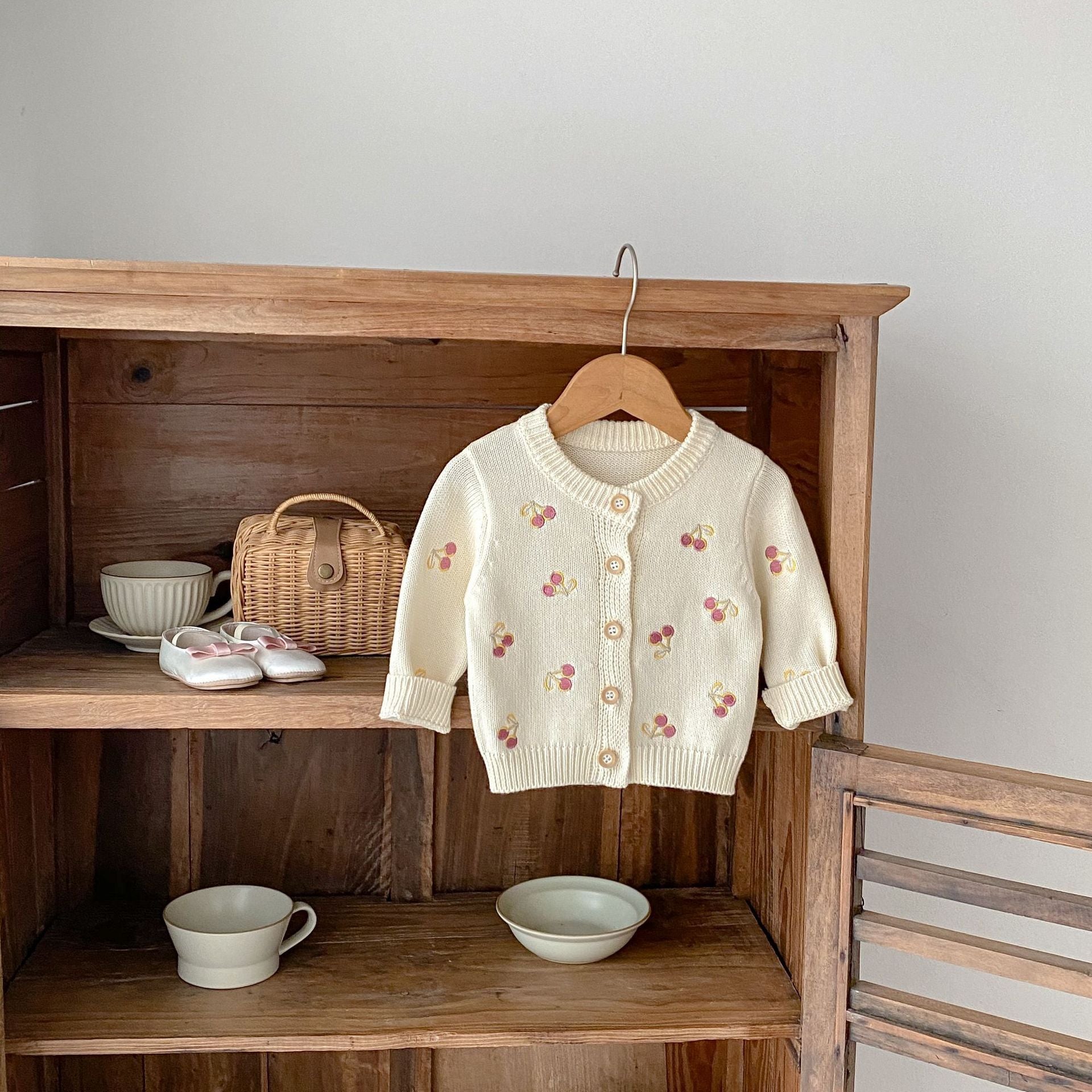 White cardigan with floral patterns hanging on a wooden shelf with various items.