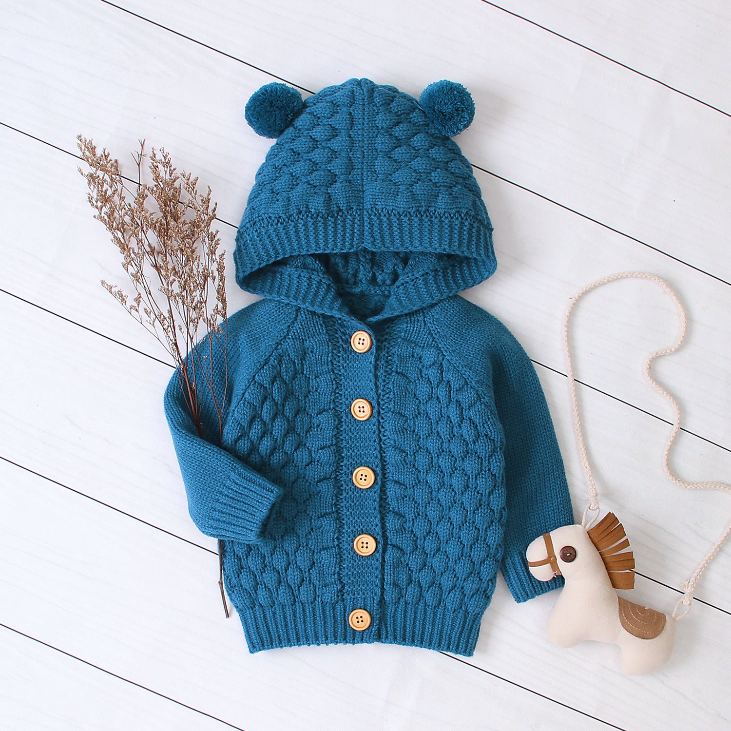 Blue knitted children's hoodie with bear ears on a white wooden floor.