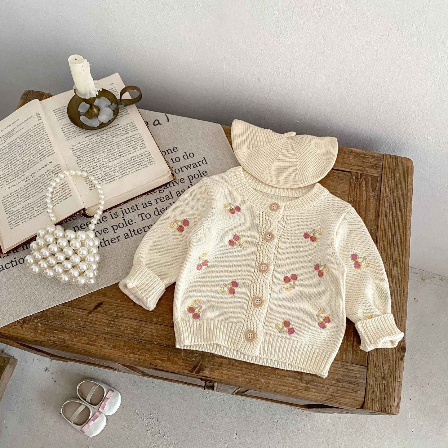 Baby sweater with cherry pattern on a wooden surface with books and shoes.