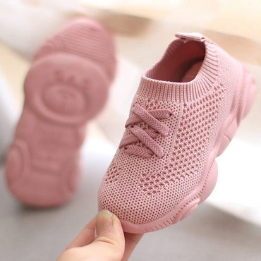 Pink knitted baby shoe held by a hand on a light background