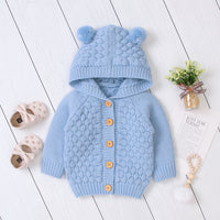 Blue knitted baby cardigan with hood on a white wooden floor.