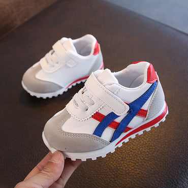 Children's sneakers with red and blue stripes held by a hand on a dark surface