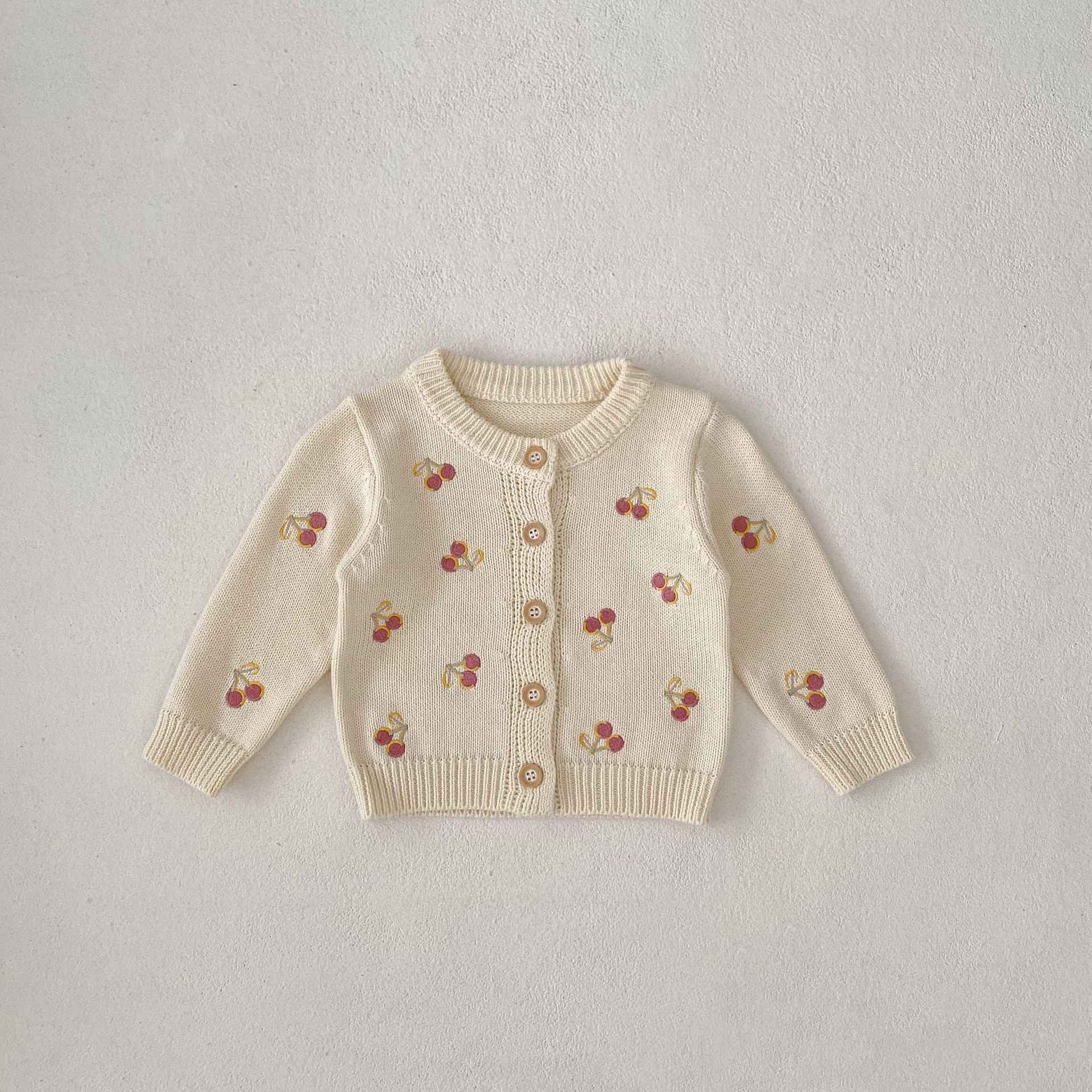 Beige cardigan with cherry patterns on a light gray background