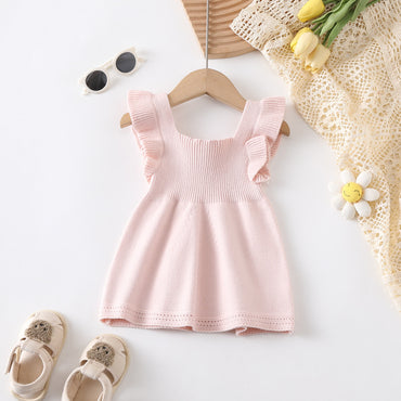 Pink baby dress on a hanger with shoes, sunglasses, and flowers on a white background