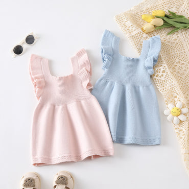 Two baby dresses, one pink and one blue, on a light surface with flowers and sunglasses.