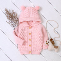 Pink knitted baby outfit with a hat and toy on a white wooden floor