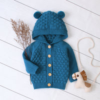 Blue knitted children's hoodie with bear ears on a white wooden floor.